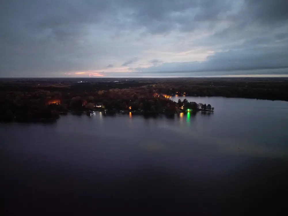 A northern Minnesota lake at dusk, with shoreline lights reflected on still water.