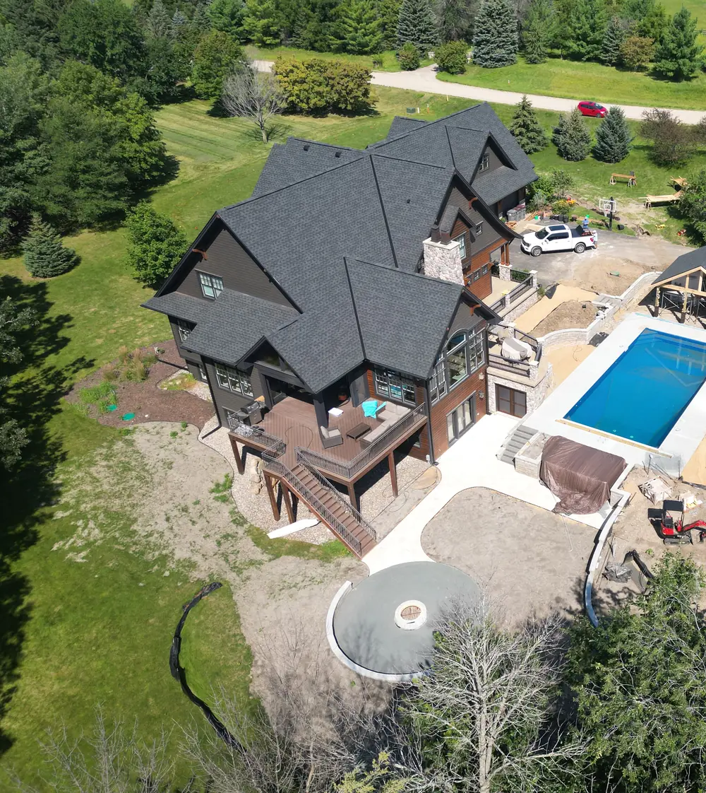 The renovated home from above, with charcoal exterior, new roof, pool and surrounding trees.