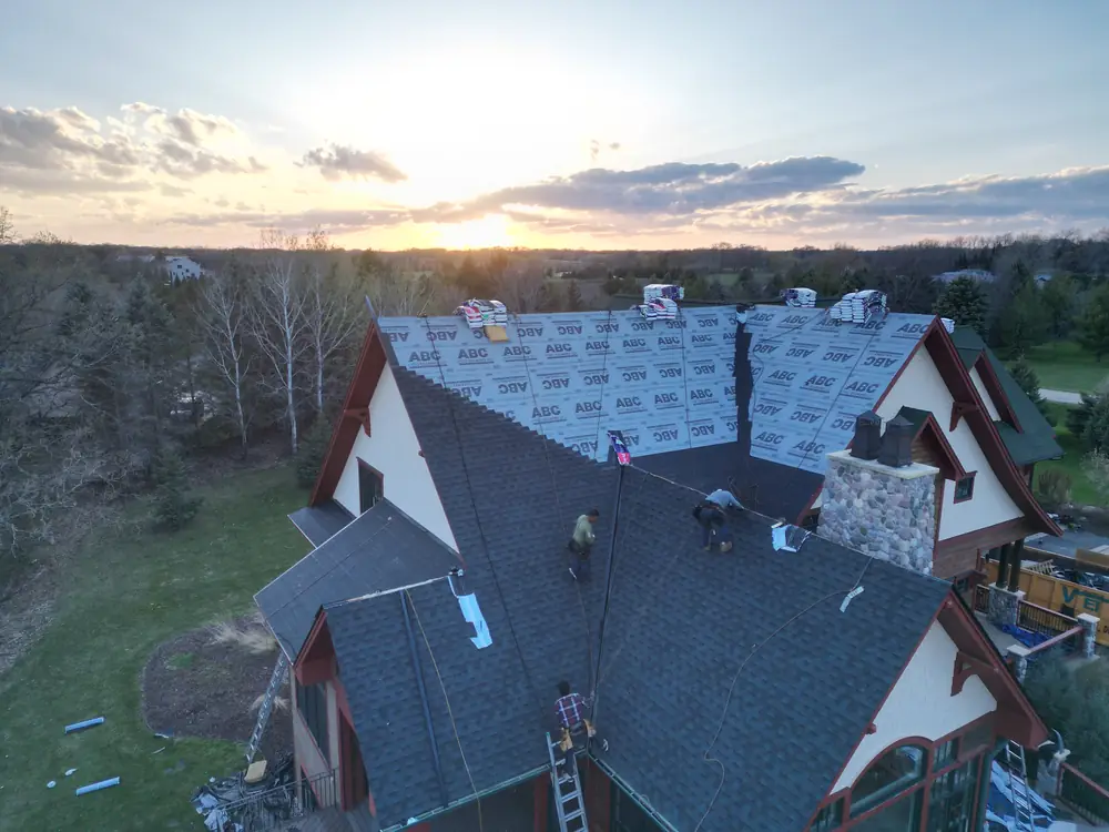 Roofers installing new shingles on the home at sunset.